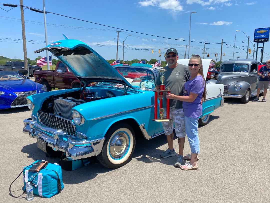 Ken and his wife holding a large trophy beside Ole' Belle at the K and H car show