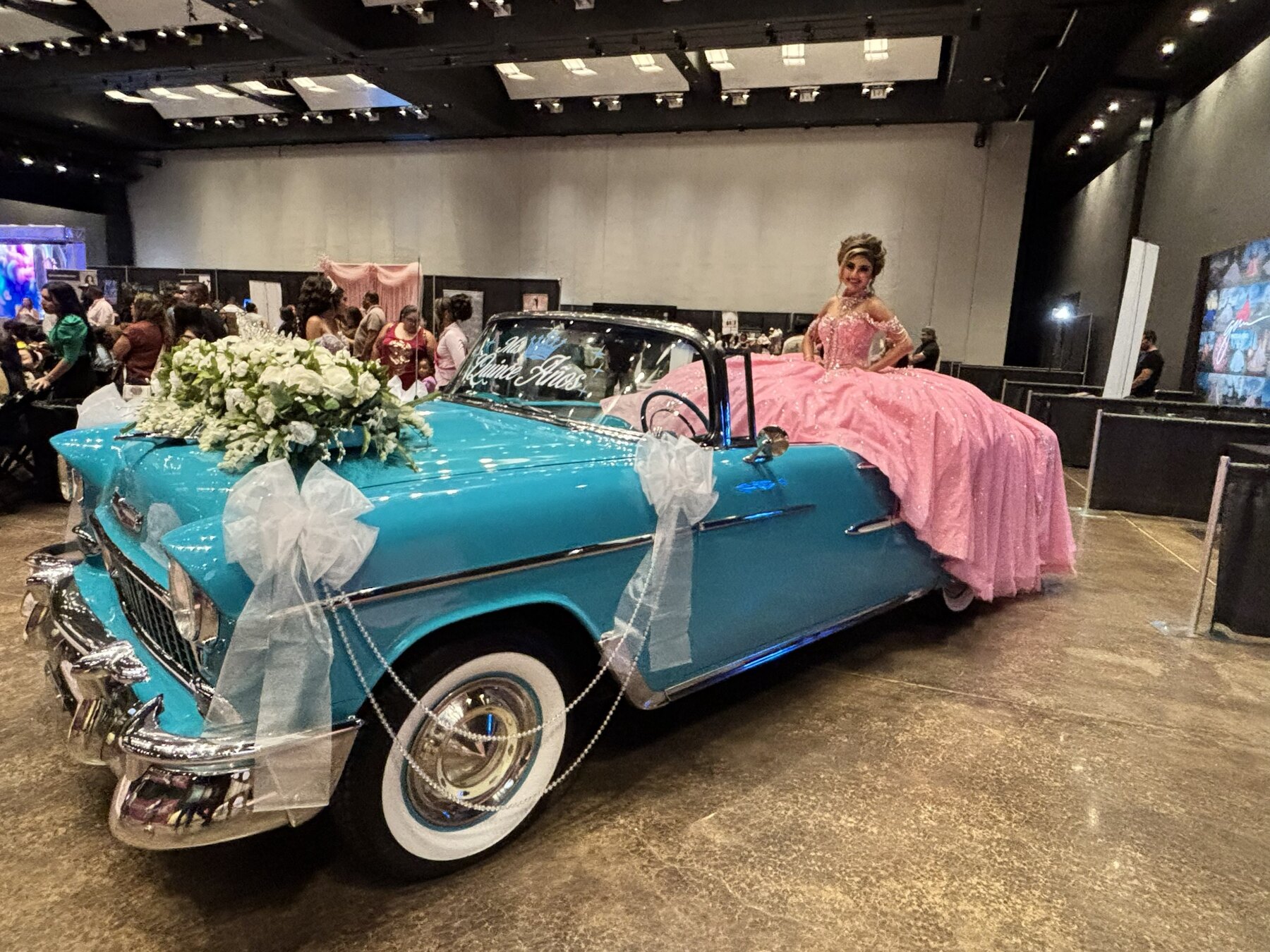 Young woman in a pink quinceañera gown posing beside decorated Ole' Belle at the Quinceañera Expo