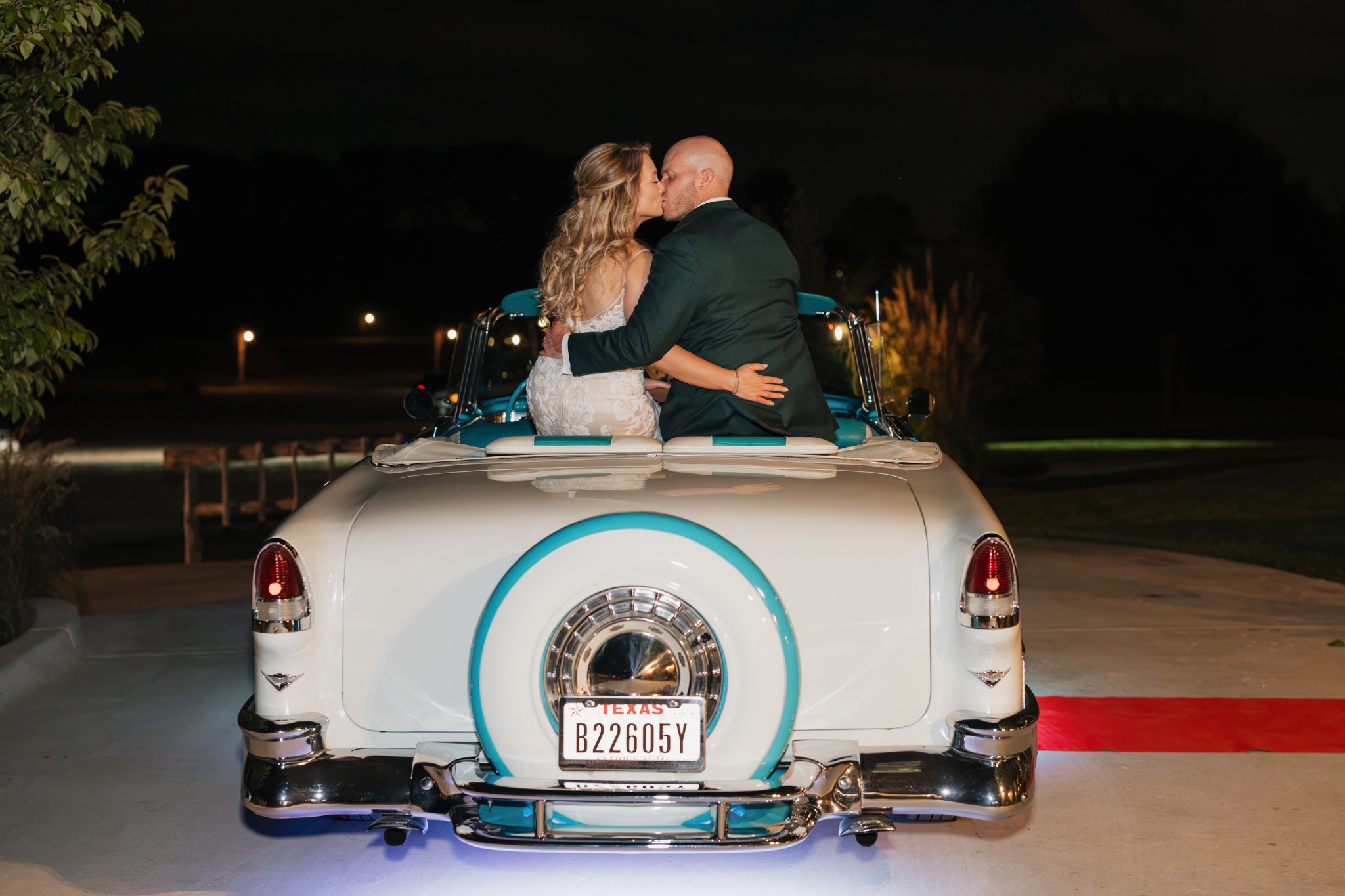 Newlyweds kissing while seated on the back of turquoise-and-white Ole' Belle at night